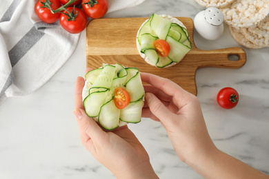 Photo of Woman holding puffed rice cake with vegetables at white marble table, top view