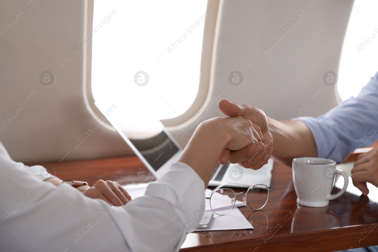 Photo of Young people shaking hands after bargaining on plane, closeup. Business deal