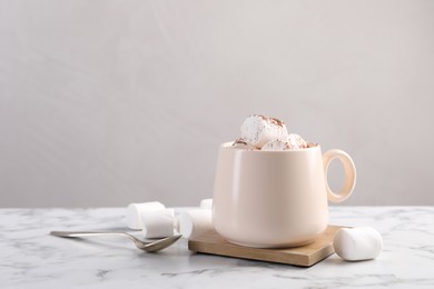 Photo of Cup of aromatic hot chocolate with marshmallows and cocoa powder served on white marble table against beige background, space for text