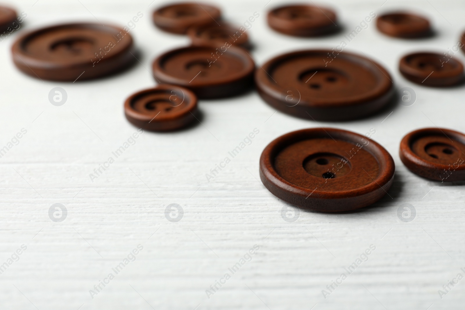 Photo of Many brown sewing buttons on white wooden background, closeup