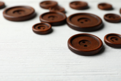 Many brown sewing buttons on white wooden background, closeup