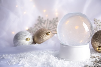 Photo of Magical empty snow globe with Christmas decorations on white fabric. Space for text