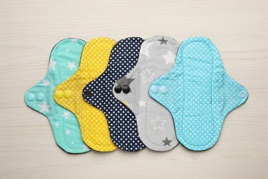 Many reusable cloth menstrual pads on white wooden table, flat lay