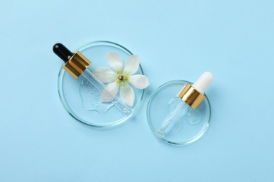 Petri dishes with samples of cosmetic oil, pipettes and beautiful flower on light blue background, flat lay