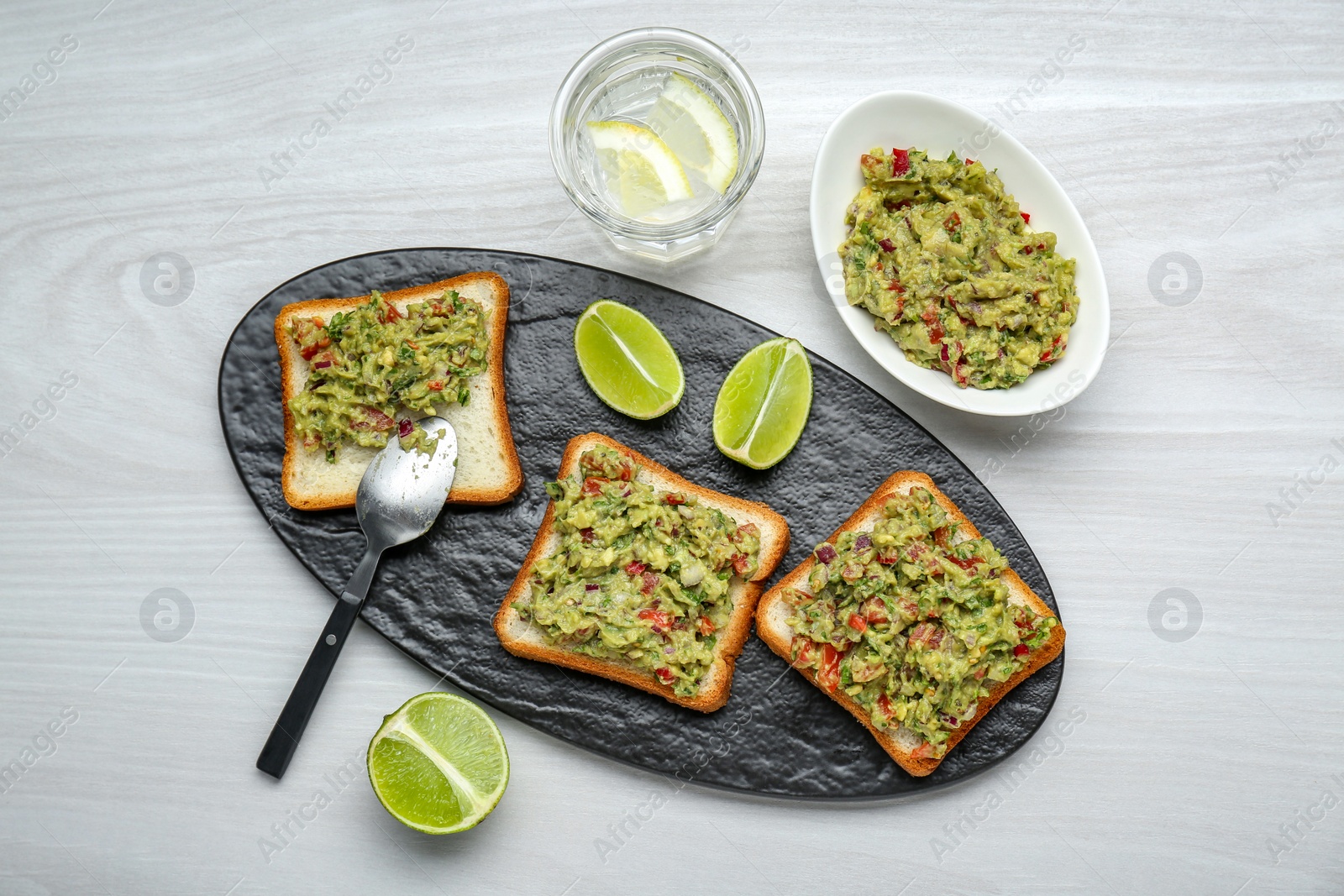 Photo of Delicious sandwiches with guacamole and lime wedges on white wooden table, flat lay