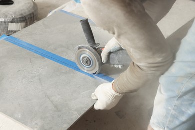 Photo of Worker cutting tile with circular saw indoors, closeup