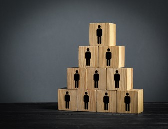 Team and management concept. Pyramid of wooden cubes with human icons on table against grey background, space for text