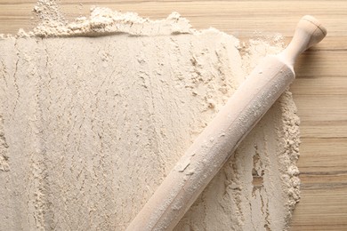 Photo of Flour and rolling pin on wooden table, top view