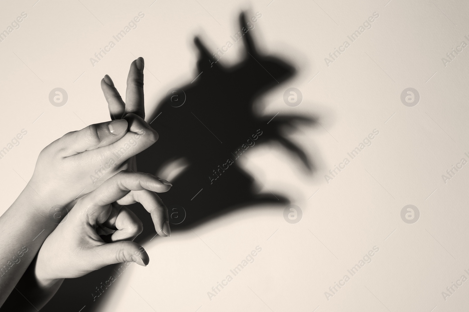 Photo of Shadow puppet. Woman making hand gesture like rabbit on light background, closeup with space for text. Black and white effect