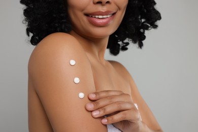 Young woman applying body cream onto arm on grey background, closeup