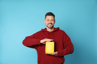 Man holding yellow container of motor oil on light blue background