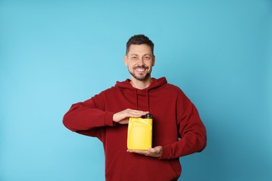 Photo of Man holding yellow container of motor oil on light blue background