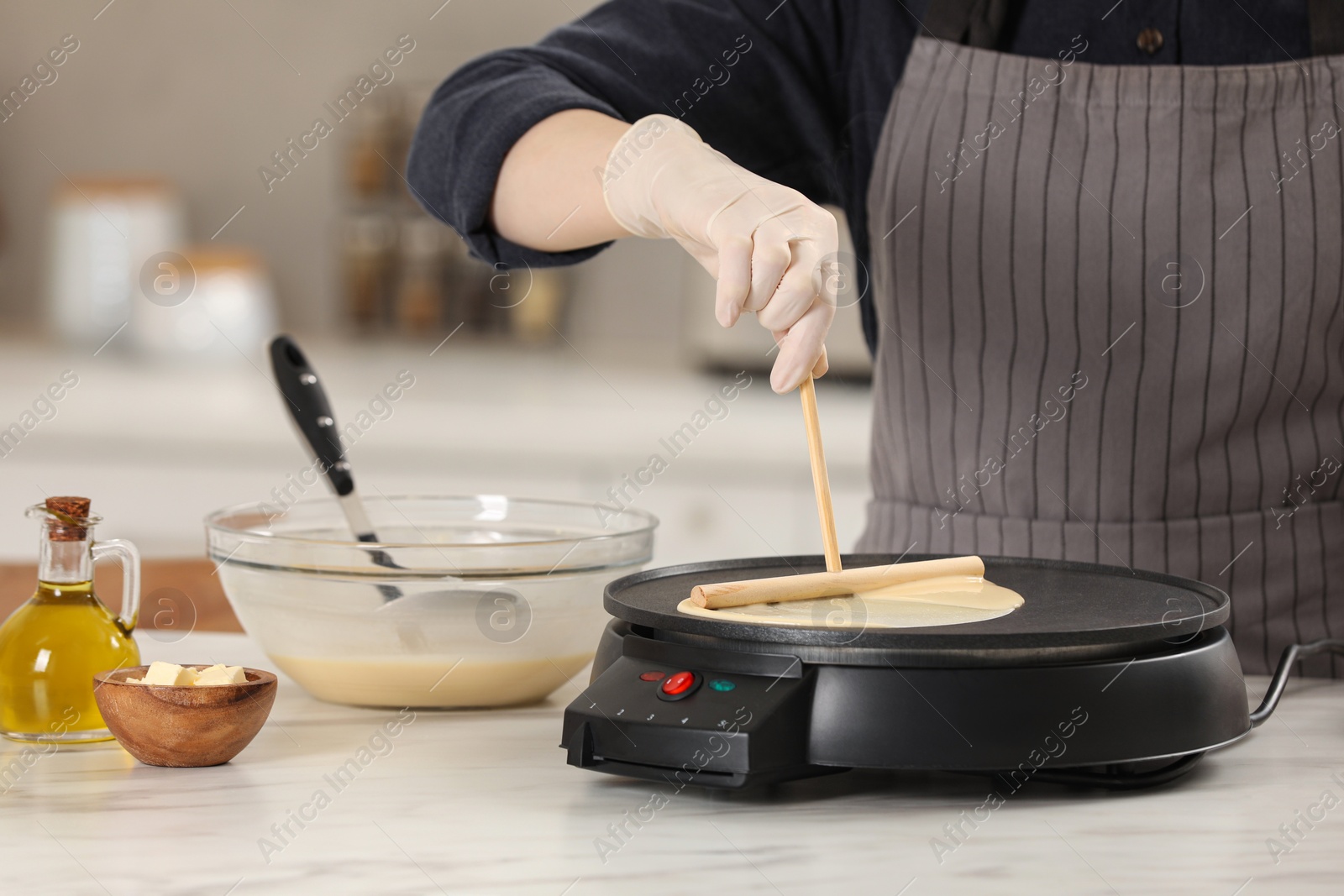 Photo of Woman cooking delicious crepe on electric pancake maker at white marble table in kitchen, closeup