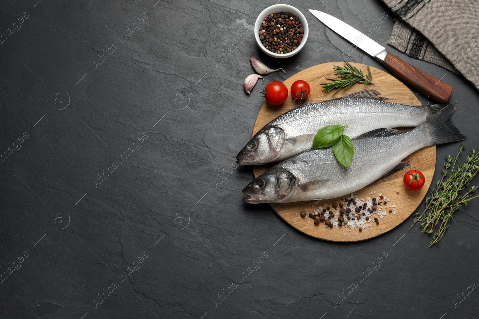 Photo of Sea bass fish and ingredients on black table, flat lay. Space for text