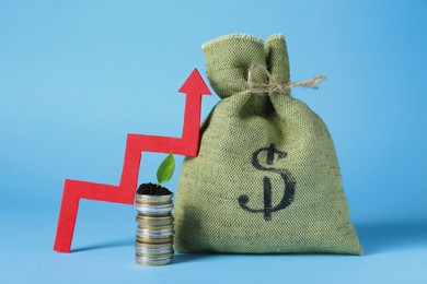 Photo of Stack of coins, green plant, up arrow and bag with money on light blue background. Profit concept