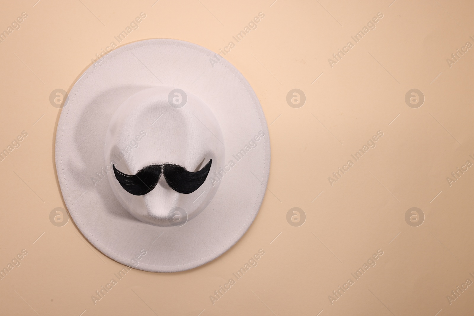 Photo of Man's face made of artificial mustache and hat on beige background, top view. Space for text