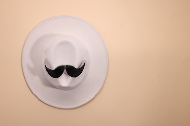 Man's face made of artificial mustache and hat on beige background, top view. Space for text