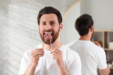 Photo of Handsome man brushing his tongue with cleaner in bathroom