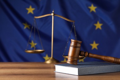Photo of Judge's gavel and book on wooden table against European Union flag. Space for text