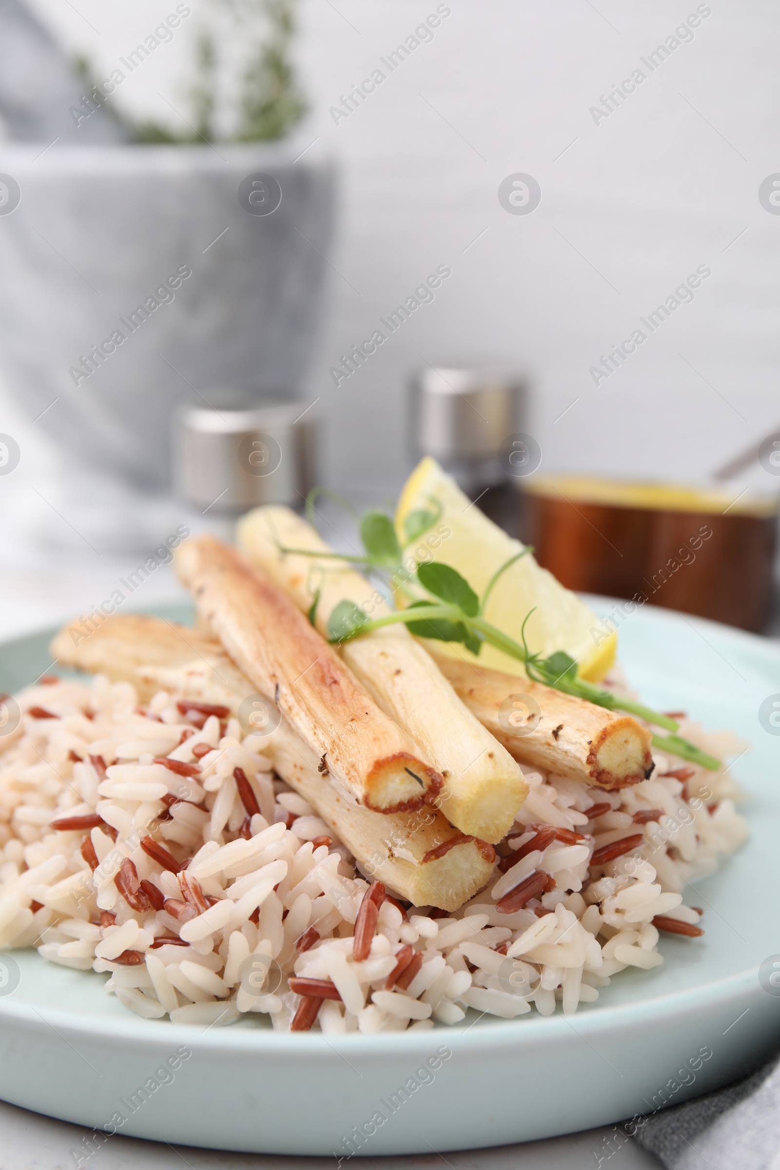 Photo of Plate with baked salsify roots, lemon and rice on table, closeup