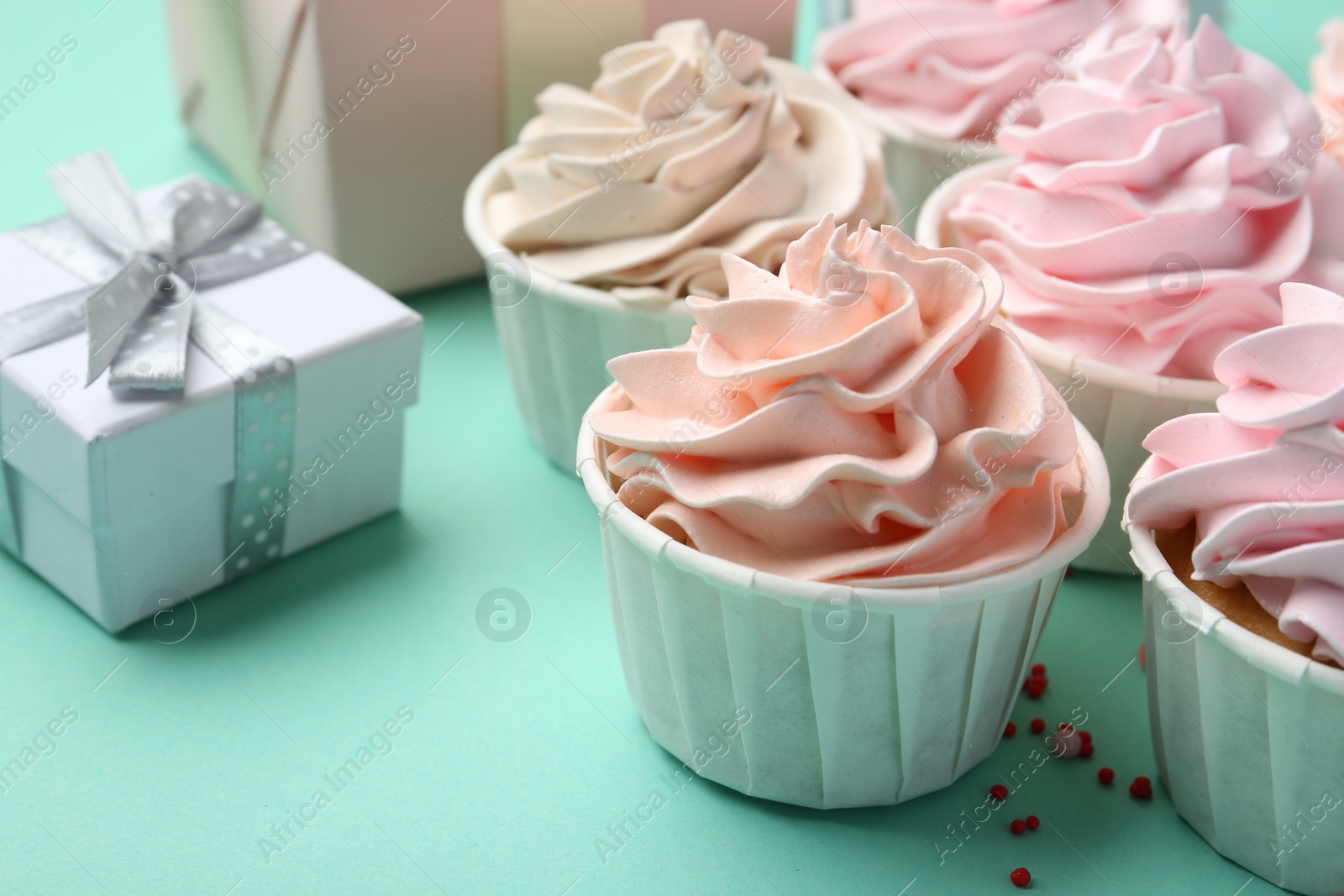 Photo of Delicious birthday cupcakes, gift boxes and sprinkles on turquoise background, closeup