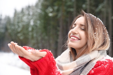 Photo of Young woman in warm clothes catching snow outdoors, space for text. Winter vacation