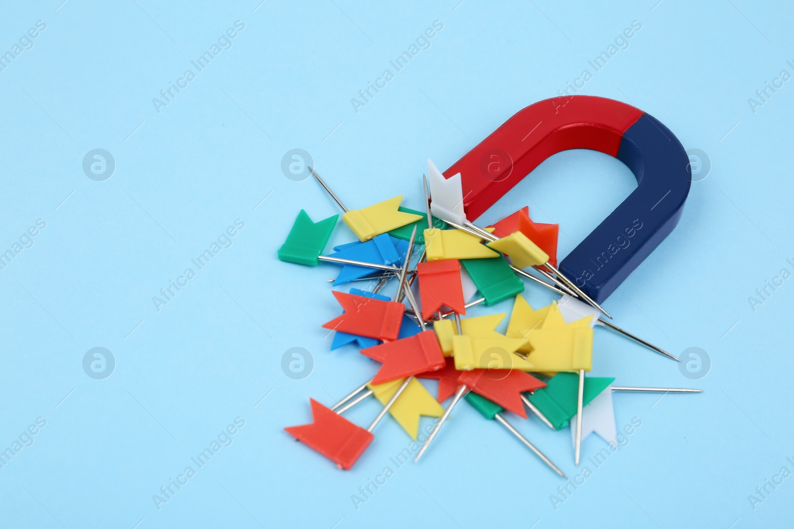 Photo of Magnet attracting colorful pins on light blue background