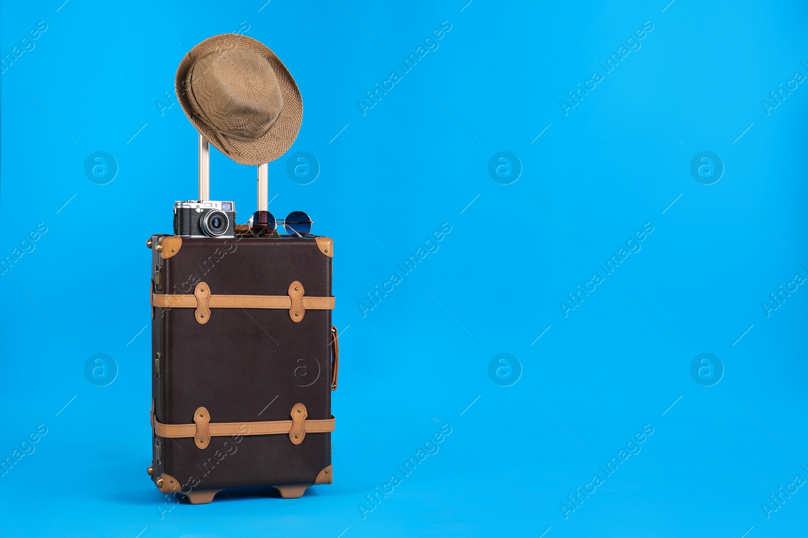 Photo of Vintage travel suitcase with hat, camera and sunglasses on light blue background, space for text. Summer vacation