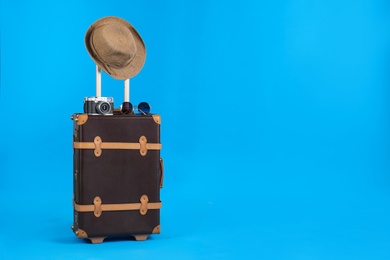 Photo of Vintage travel suitcase with hat, camera and sunglasses on light blue background, space for text. Summer vacation