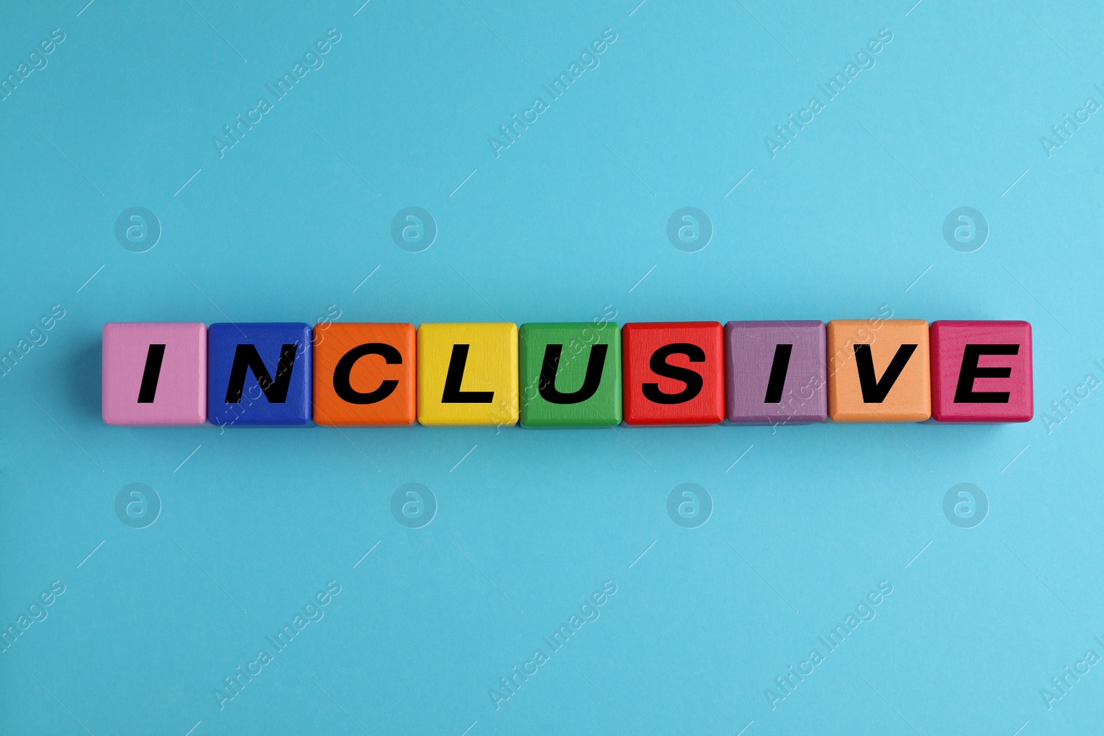 Photo of Colorful cubes with word Inclusive on light blue background, flat lay