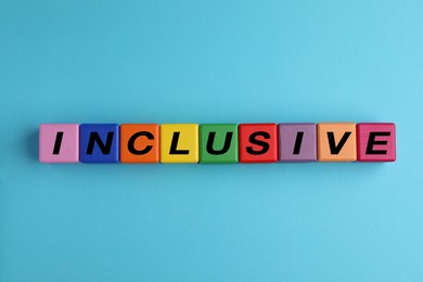 Photo of Colorful cubes with word Inclusive on light blue background, flat lay
