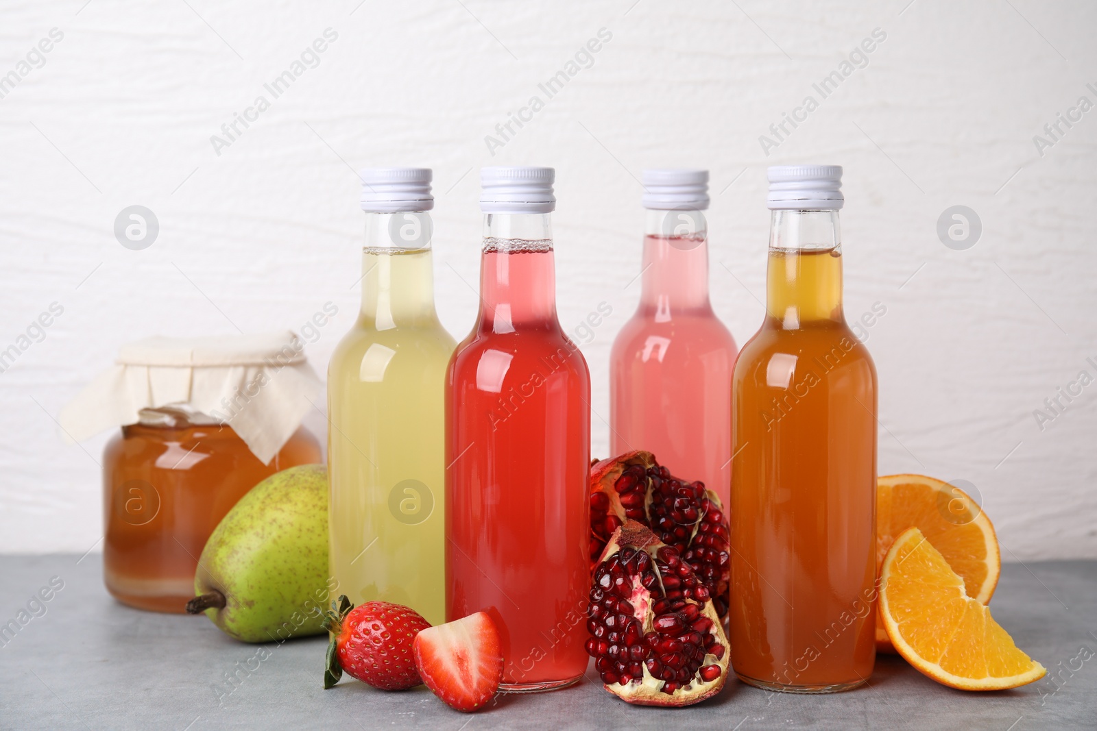 Photo of Delicious kombucha in glass bottles, jar and fresh fruits on grey table against white background