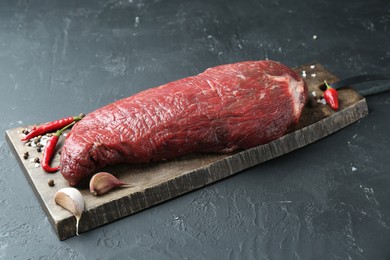 Photo of Piece of raw beef meat, garlic, chili and spices on grey textured table