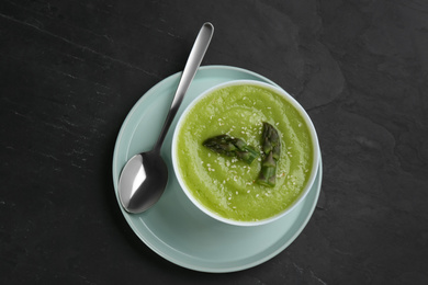 Photo of Delicious asparagus soup served on black table, top view