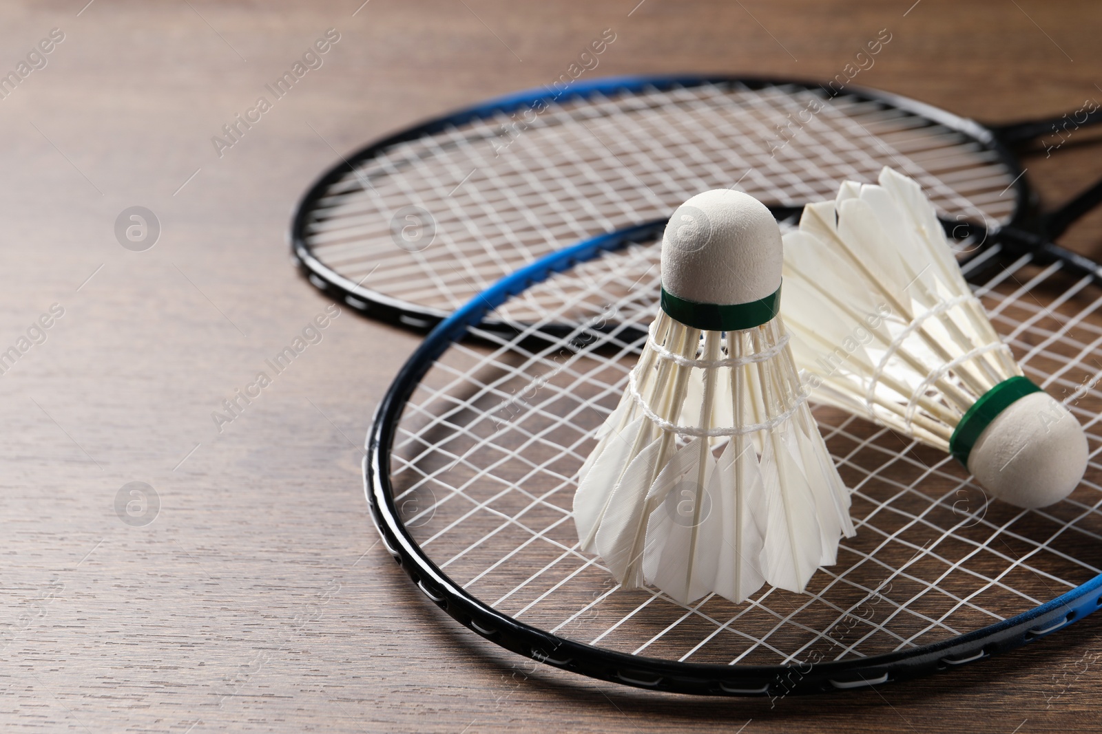 Photo of Feather badminton shuttlecocks and rackets on wooden table, closeup. Space for text