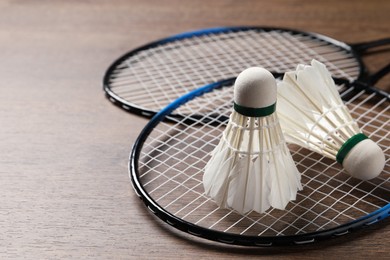 Feather badminton shuttlecocks and rackets on wooden table, closeup. Space for text