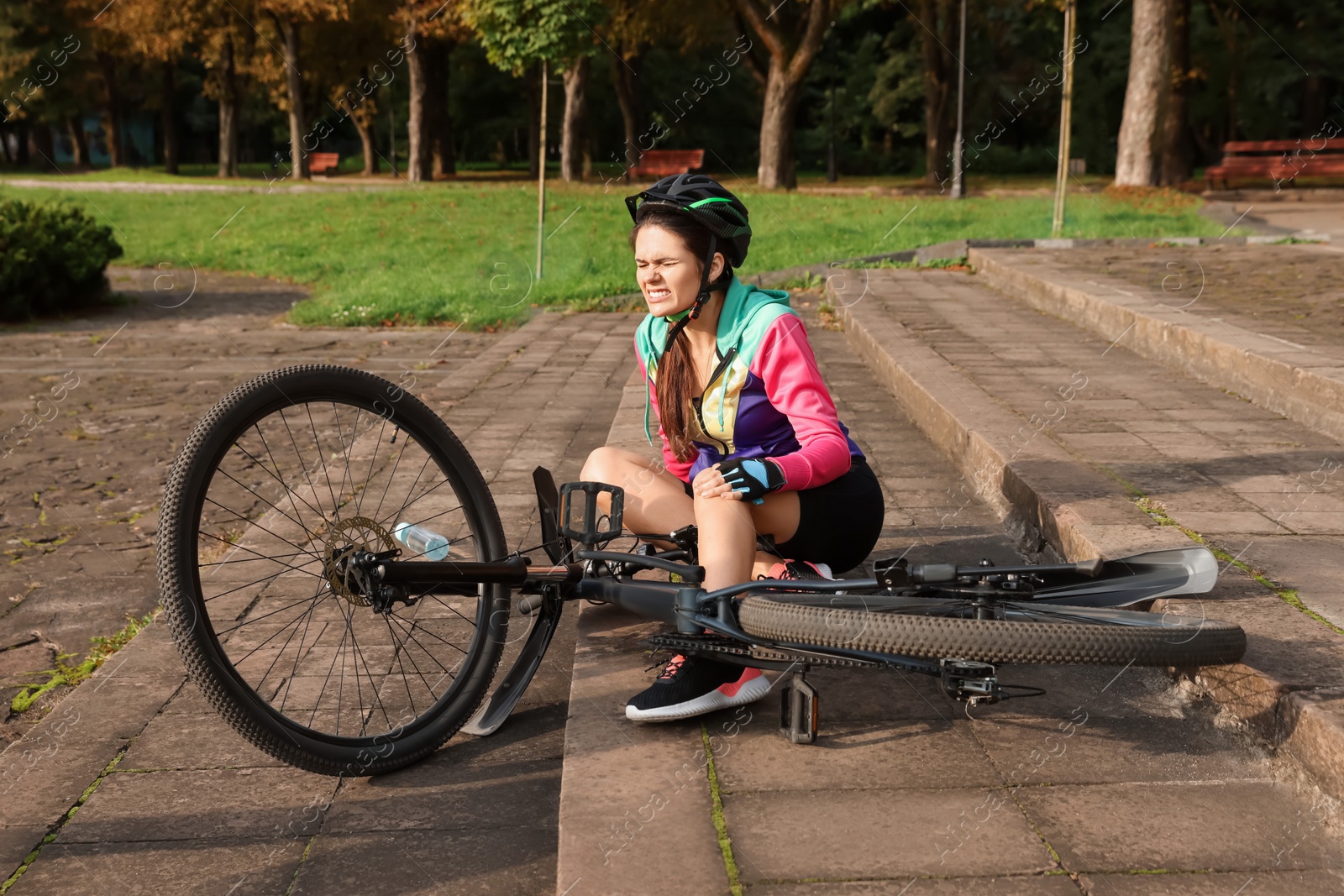 Photo of Young woman with injured knee on steps near bicycle outdoors