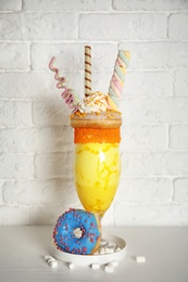 Photo of Glass of tasty milk shake with sweets on table near brick wall