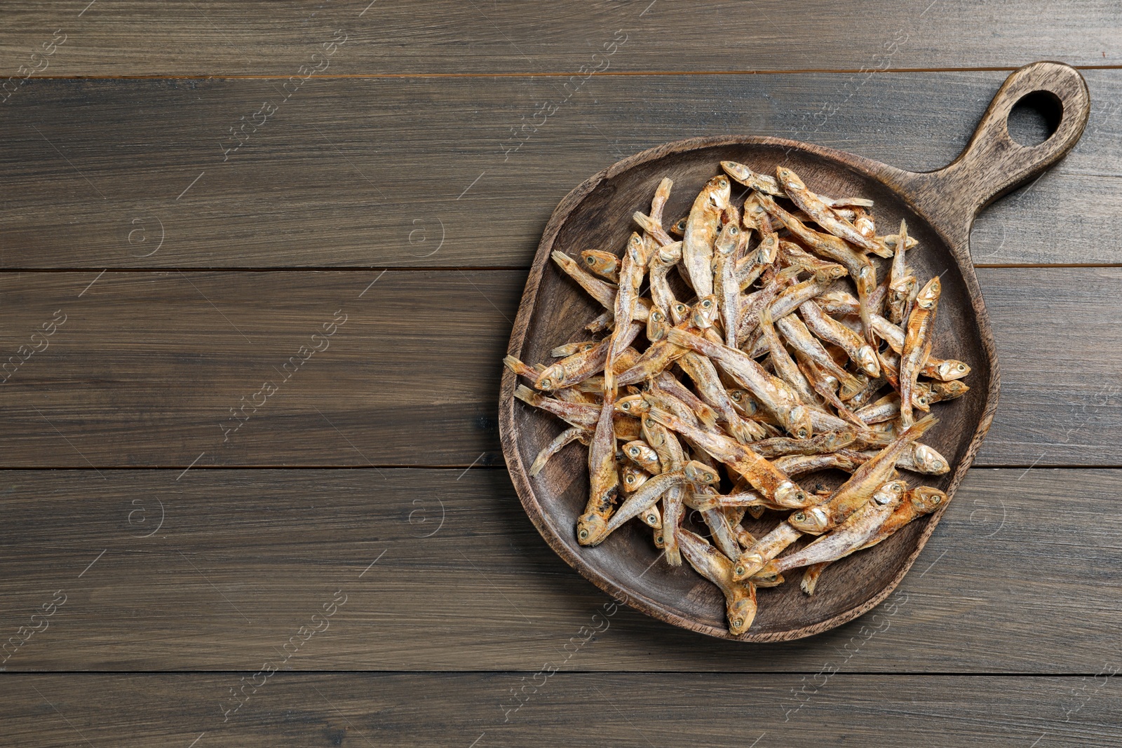 Photo of Serving board with tasty dried anchovies on wooden table, top view. Space for text