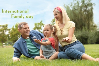 Image of Happy parents and their daughter blowing soap bubbles in park on green grass. Happy Family Day