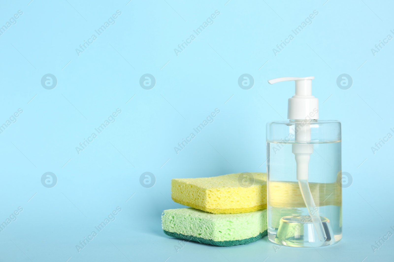 Photo of Cleaning product and sponges on light blue background, space for text. Dish washing supplies