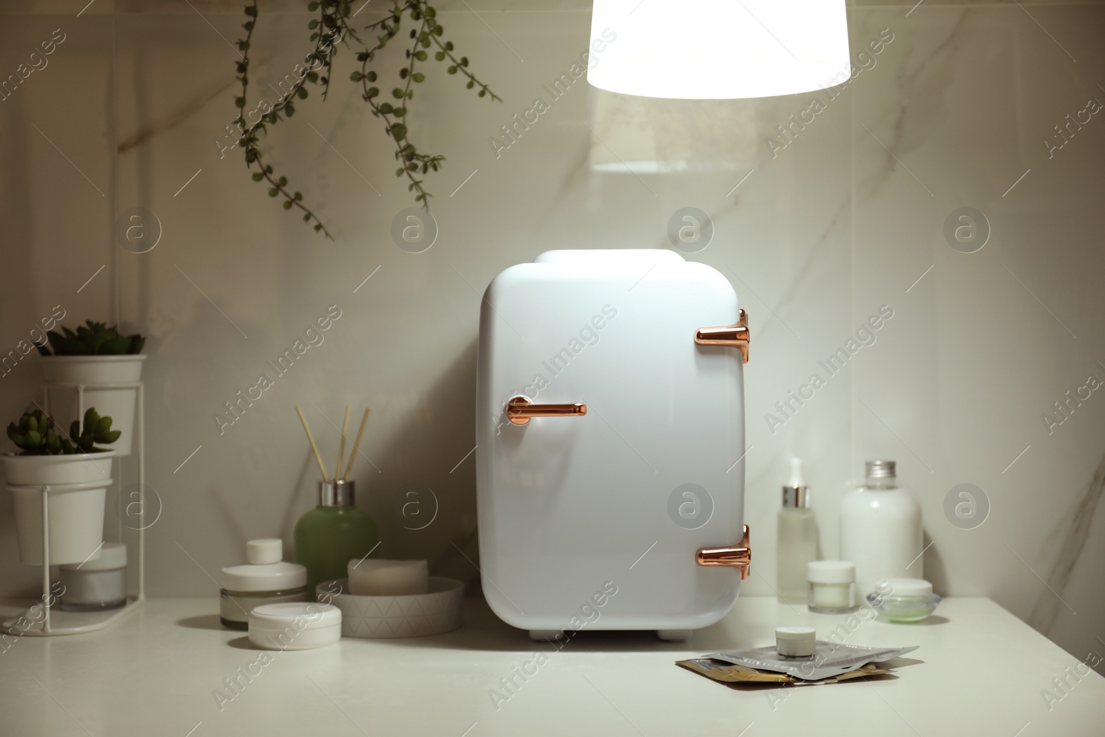 Photo of Cosmetics refrigerator and skin care products on white table indoors