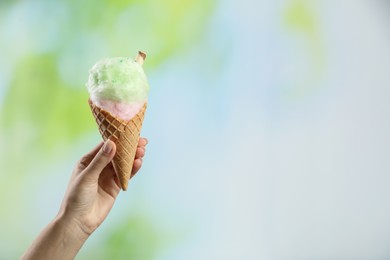 Woman holding waffle cone with cotton candy on blurred background, closeup. Space for text