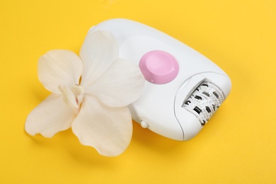 Modern epilator and orchid flower on yellow background