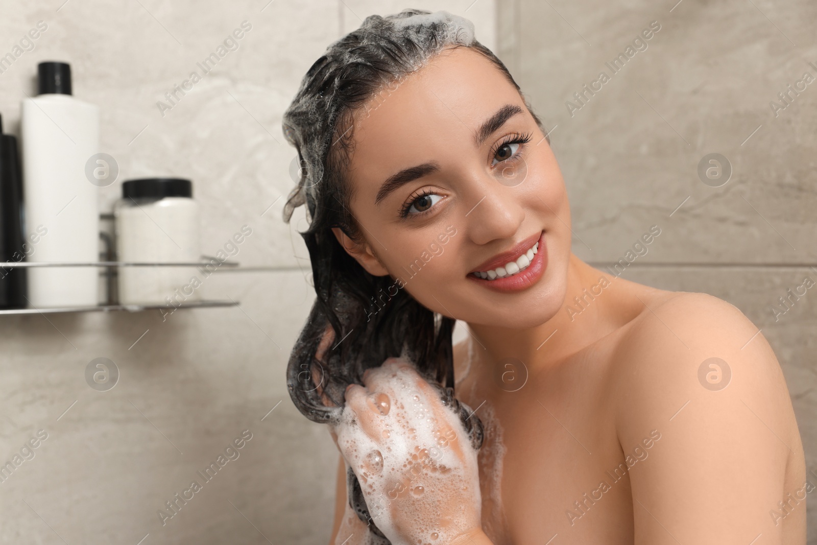 Photo of Beautiful happy woman washing hair with shampoo in shower