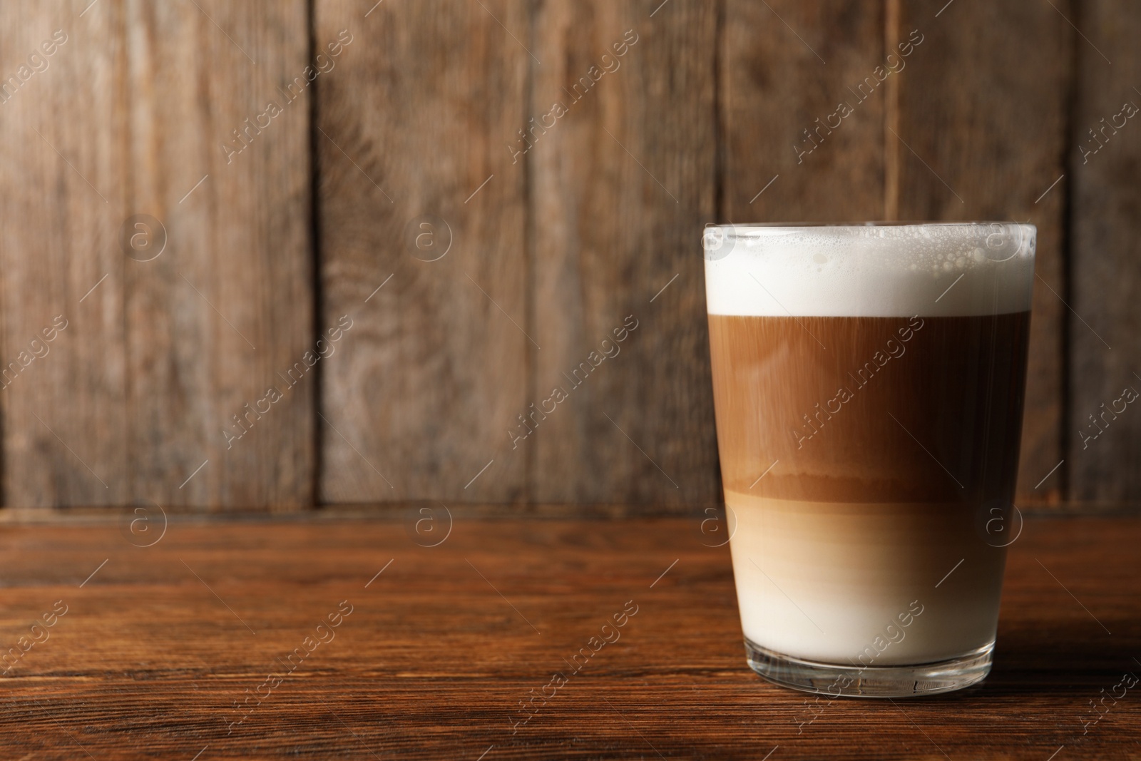 Photo of Glass of delicious layered coffee on wooden table, space for text