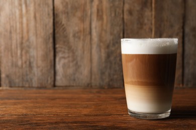 Photo of Glass of delicious layered coffee on wooden table, space for text