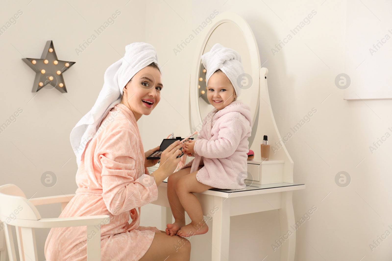 Photo of Young mother and little daughter doing makeup at dressing table