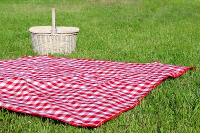 Checkered tablecloth and picnic basket on green grass outdoors