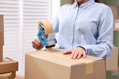 Photo of Parcel packing. Post office worker taping box indoors, closeup